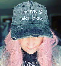 Person wearing a distressed denim cap with 'little ray of pitch black' text, pink hair, blurred background