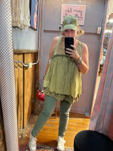 Girl in a yellowish tank top taking a selfie in front of mirror wearing a hat and green pants and white sneakers