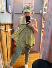 Girl in a yellowish tank top does taking a selfie in front of mirror wearing a hat and green pants and white sneakers