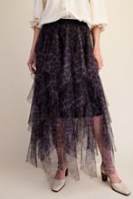 A model wearing a tiered tulle midi skirt with a dark purple and black leopard print pattern, styled with a cream blouse and beige heels against a solid beige background.