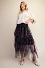 A woman models a high-low tulle skirt with a dark purple and black leopard print, styled with a cream blouse and beige heels against a solid beige studio background.
