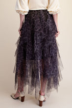 A model from the back wearing a dark purple and black leopard-print tulle skirt with layered ruffles, paired with a cream blouse and beige heeled sandals, against a solid beige background.