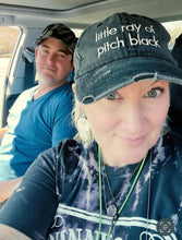 Two people sitting inside a car, with one wearing a cap with text.