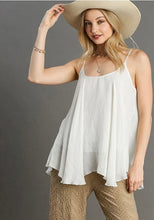 Woman wearing a white sleeveless top and beige pants with a wide-brimmed hat against a gray background