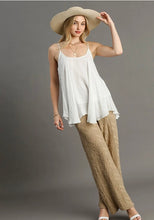 Woman wearing a white top and beige pants with a wide-brimmed hat against a gray background