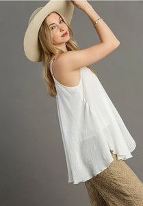 Woman wearing a white sleeveless top and beige hat against a gray background