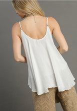 Woman wearing a white sleeveless top and beige pants against a gray background