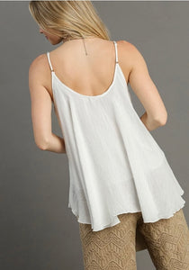 Woman wearing a white sleeveless top and beige pants against a gray background