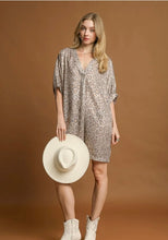 Woman wearing a patterned dress holding a white hat against a brown background leopard print
