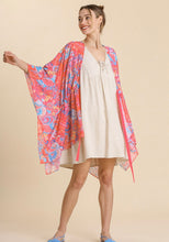 Woman wearing a white dress with a colorful floral kimono over it on a beige background