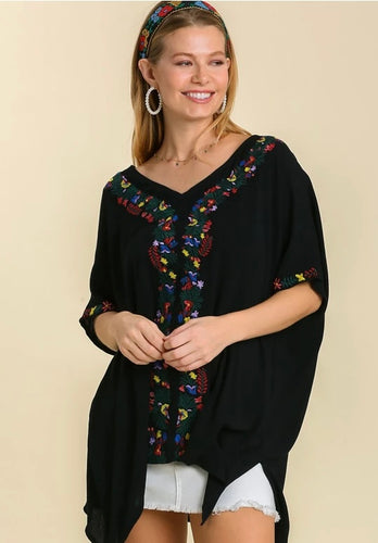 Woman wearing a black embroidered top on a beige background