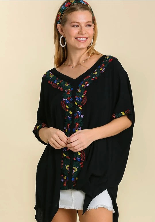 Woman wearing a black embroidered top on a beige background