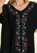Black top with colorful floral embroidery on a neutral background