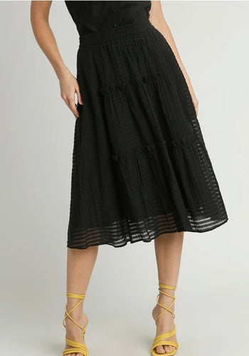 Black tiered skirt worn by a person on a plain background