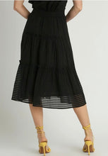 Black tiered skirt worn by a person on a plain background