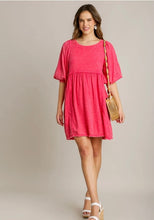 Woman wearing a pink dress holding a wooden handbag against a plain background