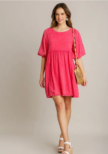 Woman wearing a pink dress holding a wooden handbag against a plain background