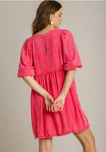 Woman wearing a pink dress with puff sleeves on a plain background