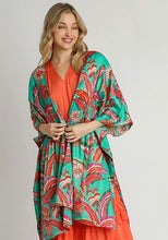 Woman wearing a colorful floral kimono over an orange dress on a plain background