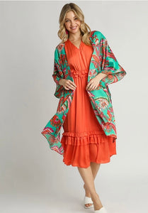Woman wearing an orange dress with a floral kimono over it on a gray background