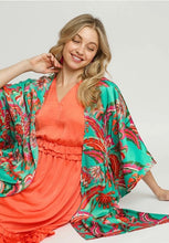 Woman wearing a coral dress with a green floral kimono over it on a white background