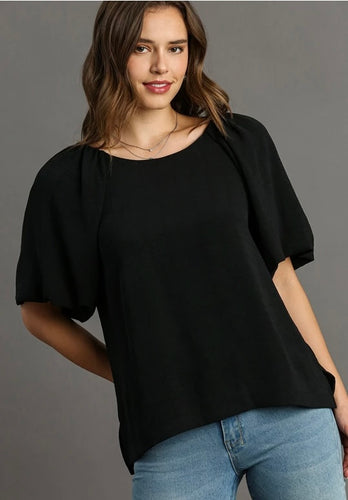 Woman wearing a black top and blue jeans against a gray background