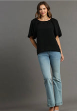 Woman wearing a black top and light blue jeans against a gray background