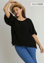Woman wearing a black top and blue pants with a straw hat on a plain background