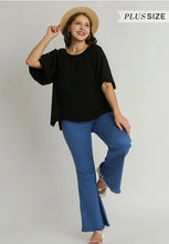 Woman wearing a black top and blue jeans with a straw hat on a plain background