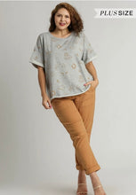 Woman wearing a gray patterned top and brown pants on a plain background with 'Plus Size' text.