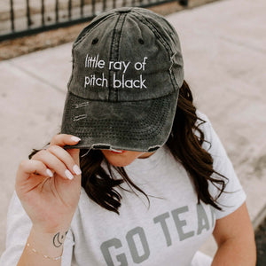 Person wearing a distressed black baseball cap with text and a white t-shirt with 'GO TEAM' printed on it.