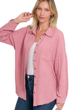Woman wearing a pink button-up shirt over a white top and blue jeans on a white background