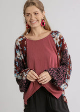 Woman wearing a pink top and floral and leopard print cardigan on a plain background