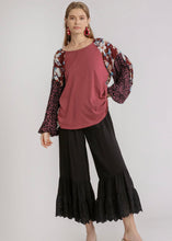 Woman wearing a pink top and black pants with floral sleeves on a white background