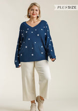 Woman wearing a navy blue sweater with star patterns and white pants on a beige background