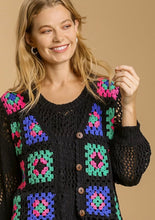 Woman wearing a black cardigan with colorful geometric patterns on a beige background
