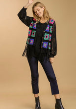 Woman wearing a black crochet cardigan with colorful patterns on a beige background