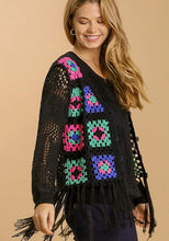 Woman wearing a black crochet cardigan with colorful square patterns on a beige background