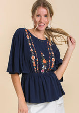 Woman wearing a navy blue top with floral embroidery on a beige background