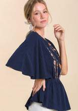 Woman wearing a navy blue top with floral patterns on a beige background