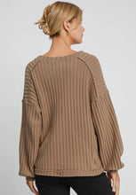 Woman wearing a brown ribbed sweater against a plain background