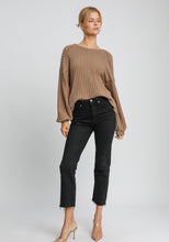 Woman wearing a brown ribbed sweater and black jeans on a white background