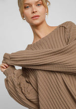 Woman wearing a brown ribbed sweater against a plain background