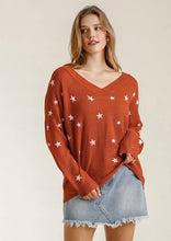 Woman wearing a rust-colored sweater with star patterns and denim shorts on a beige background