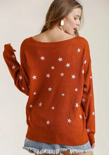 Woman wearing a rust-colored sweater with star patterns on a plain background