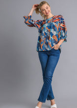 Woman wearing a colorful patterned blouse and blue jeans on a gray background