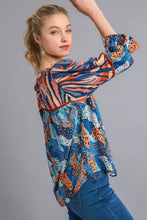 Woman wearing a colorful patterned blouse with ruffled sleeves on a gray background