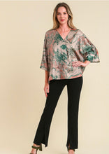 woman wearing a tan and green satin top against a tan background short sleeves in black pants