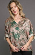 woman wearing a tan and green satin top against a grey background short sleeves
