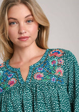 Woman wearing a green floral embroidered blouse against a plain background